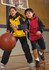 A boy in a red rain jacket and a girl in a yellow rain jacket play basketball indoors. Both jackets have branding.