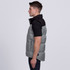A grey puffer vest with a black collar, featuring a logo and side pockets, worn by a model in profile.