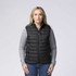 A black padded baffle vest features zippered pockets and is worn over a grey long-sleeve shirt.