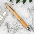 A bamboo pen with metal accents resting on a textured surface near a keyboard and greenery.