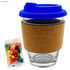 A glass coffee cup with a royal blue lid and a cork band, accompanied by a packet of colourful jelly beans.