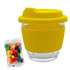 A yellow glass coffee cup with a silicone sleeve and lid, alongside a packet of colourful jelly beans.