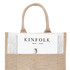 A jute bag in natural brown with handles, featuring a magazine partially visible in the front pocket and a logo.