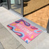 A colourful mat with a swirling pattern and a welcoming design, placed at an entrance.
