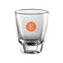 A clear glass shot glass with a solid base and an orange circular logo containing the letter "E."