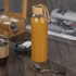 A drink bottle in a clear design with a bamboo lid and a rope handle, filled with orange liquid.