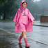 A pink reusable PEVA rain poncho with a hood, featuring a logo, worn by a person in the rain.