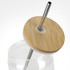 A glass tumbler with a bamboo lid and metal straw. The tumbler is partially filled with water.