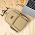 A canvas laptop backpack in beige with multiple pockets, placed on a wooden surface beside glasses and a laptop.