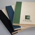 A set of three notebooks in black, dark green, and blue, featuring a logo on the front cover.
