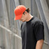 An orange organic cotton twill cap worn by a person in a black t-shirt, standing beside a metallic structure.