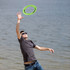 A man in sunglasses reaches for a green frisbee by the water. The background features a serene beach scene.