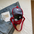 A red canvas shoulder bag with a grey interior, containing a drink bottle and other items, sits on a bed.