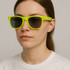 Bright yellow glow-in-the-dark sunglasses with dark lenses, worn by a model against a neutral background.
