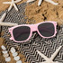 A pair of pink glow-in-the-dark sunglasses resting on a sandy surface, surrounded by starfish and seashells.