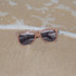 Coffee fibre sunglasses in a brown hue resting on sandy beach, with gentle waves in the background.