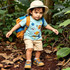 A child wearing a beige PVC safari hat and a blue T-shirt, walking on a forest trail with a small orange backpack.