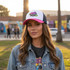A Premium Vintage Trucker Hat in pink and white with a logo, worn by a woman in a denim jacket outdoors.