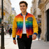 A vibrant unisex polyester spandex track jacket featuring rainbow colours and a logo, worn by a smiling individual in a city street.