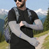 A man wearing grey long sleeve sun protective fingerless gloves, hiking in a mountainous landscape with a backpack.