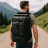 A black convertible backpack duffel bag worn on a man's back, set against a mountainous landscape.