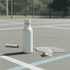 A drink bottle in white rests on a tennis court beside a racquet and shuttlecock. It features a logo.
