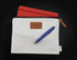 A cream conference bag featuring a brown logo patch, a red tablet cover, and a blue pen.
