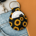 A Neoprene keychain with a sunflower design, featuring a circular compartment and a metal key ring.