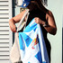 A woman holding a light blue beach towel with a logo, preparing to place it in a tote bag.