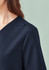 A dark navy V-neck scrub top with a subtle design detail at the shoulder, featuring a branding logo.