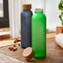 A drink bottle in frosted green glass with a wooden lid, next to a frosted grey bottle, on a wooden surface.