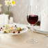 A tulip-shaped wine glass filled with red wine, set beside a plated dish with garnishes, on a elegantly arranged table.