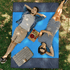 A blue polyester picnic blanket laid out on grass, featuring two people relaxing on it, with picnic items nearby.