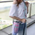 A drink bottle carrier bag in pink and purple, featuring a phone pocket, worn over the shoulder by a person.