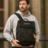 A man in a grey hoodie holds a black camouflage Flap Laptop Backpack with a logo on the front.