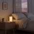 A foldable lantern in white emits a warm glow on a bedside table next to a glass of water and a small plant.