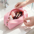 A pink silicone square cosmetic bag with makeup brushes, sponges, and a bottle inside, held by a person.