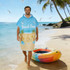 A blue and beige poncho towel with a beach design, featuring a hood and no pockets, against a coastal background.