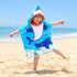 A hooded change towel featuring a blue shark design, with a child standing on the beach. It has a logo on it.