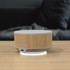 A wireless charging speaker with a bamboo design and white accents, featuring buttons and a branding logo.