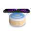 A bamboo-textured wireless charging speaker with a glowing blue top and a smartphone placed above it.