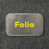 A metallic rectangular container with a brushed finish and a yellow logo. The background is a textured dark fabric.
