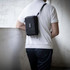 A black toiletry bag is worn crossbody by a person, showcasing its sleek design and compact size.