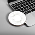A round, white wireless charger with a dotted pattern, placed next to a laptop keyboard. The charger has a metallic edge.