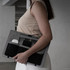 A clipboard in grey and black held by a woman, featuring pockets for devices like a phone and earphones.