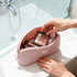 A pink silicone organiser pouch containing makeup brushes, a palette, and various beauty products beside a sink.