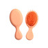A mini paddle brush in a soft peach colour with plastic bristles and an ergonomic handle. It has a simple logo.