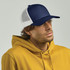 A navy and white trucker cap is worn by a man in a yellow hoodie, featuring a mesh back and a solid front.