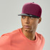 A cap featuring a burgundy front panel and a black peak, worn by a model in an orange shirt.