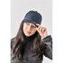 A navy trucker cap rests on the head of a woman with long black hair against a neutral background. The cap features a logo.